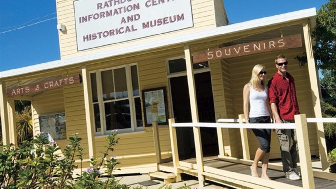 Two people walk by exterior of Rathdowney Visitor Information Centre in historic wooden building