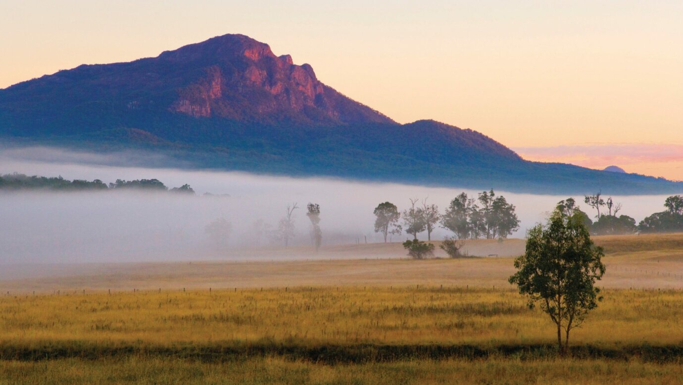 Mount Maroon with base shrouded in fog and farmlands in foreground.