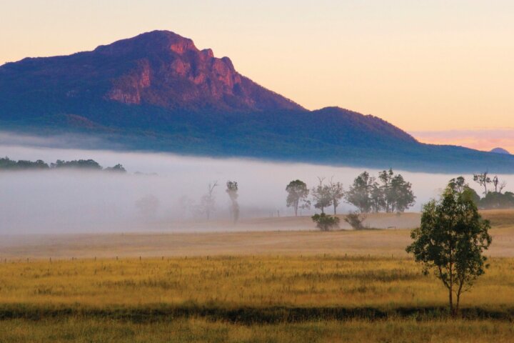 Mount Maroon with base shrouded in fog and farmlands in foreground.