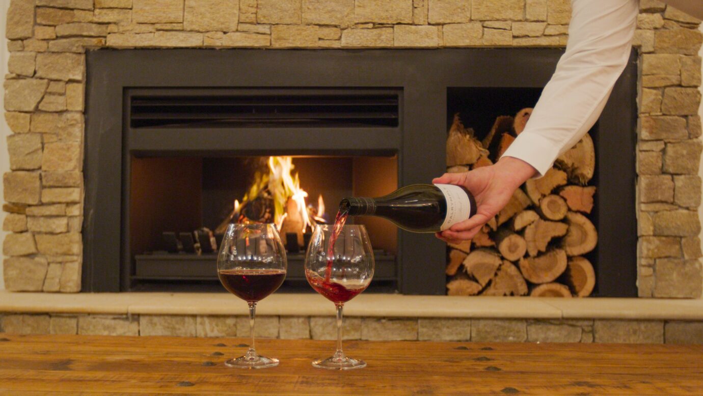 A waiter pours a glass of red in front of a roaring stone fireplace at Hazelwood Estate