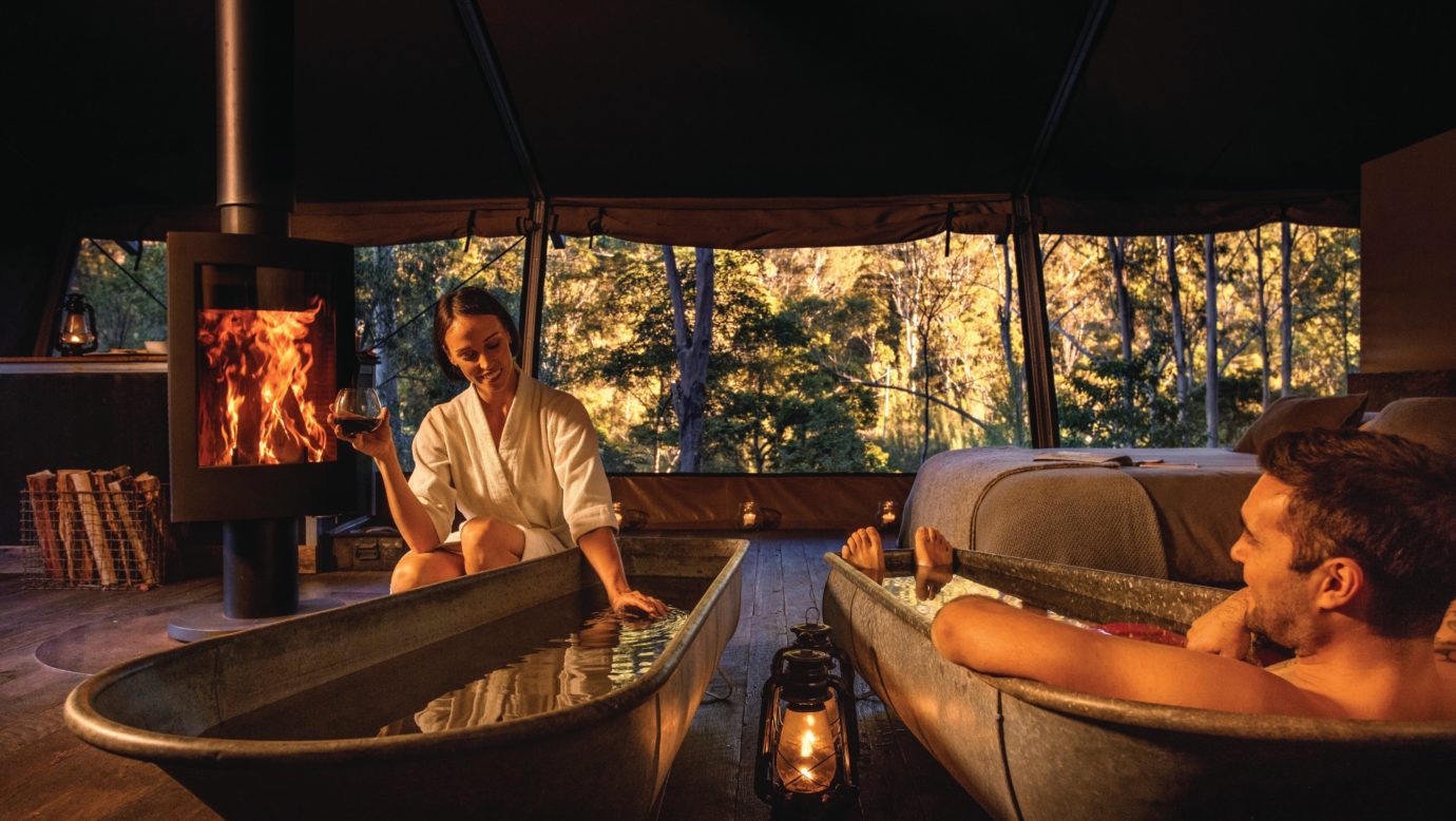 Couple enjoying bath by the fire inside safari tent with view to the natural environment.