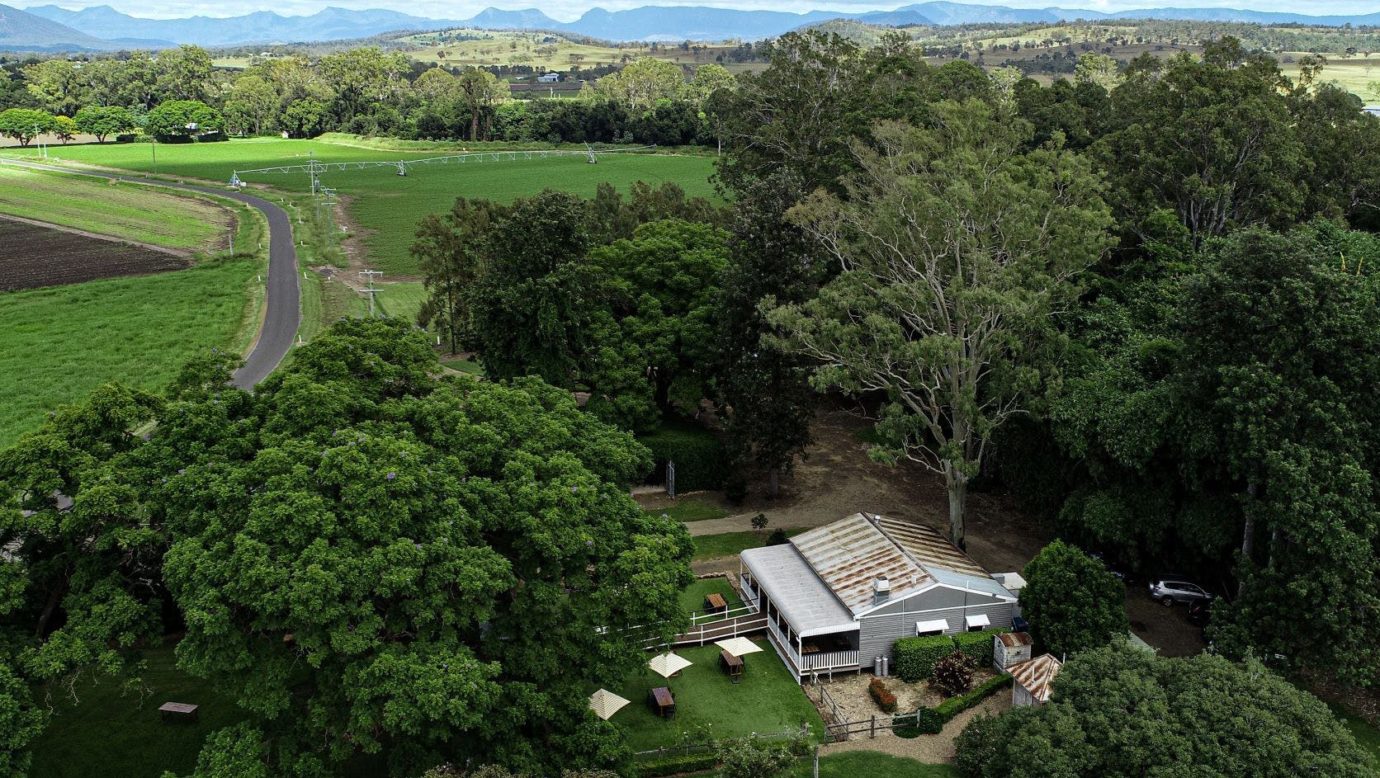 An aerial view of the cottage-style-cafe amongst large trees looking across farms to the mountains.