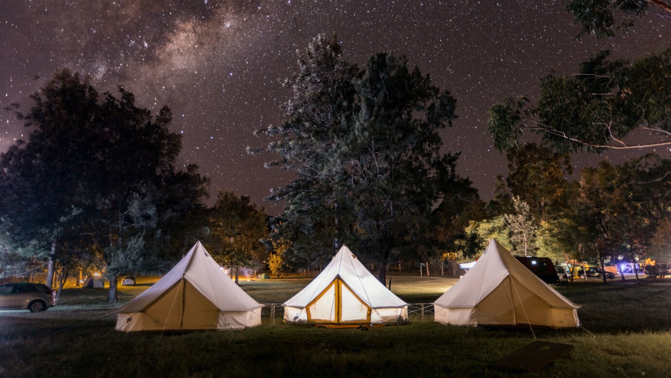3 bell tents on grass with a starry night sky.