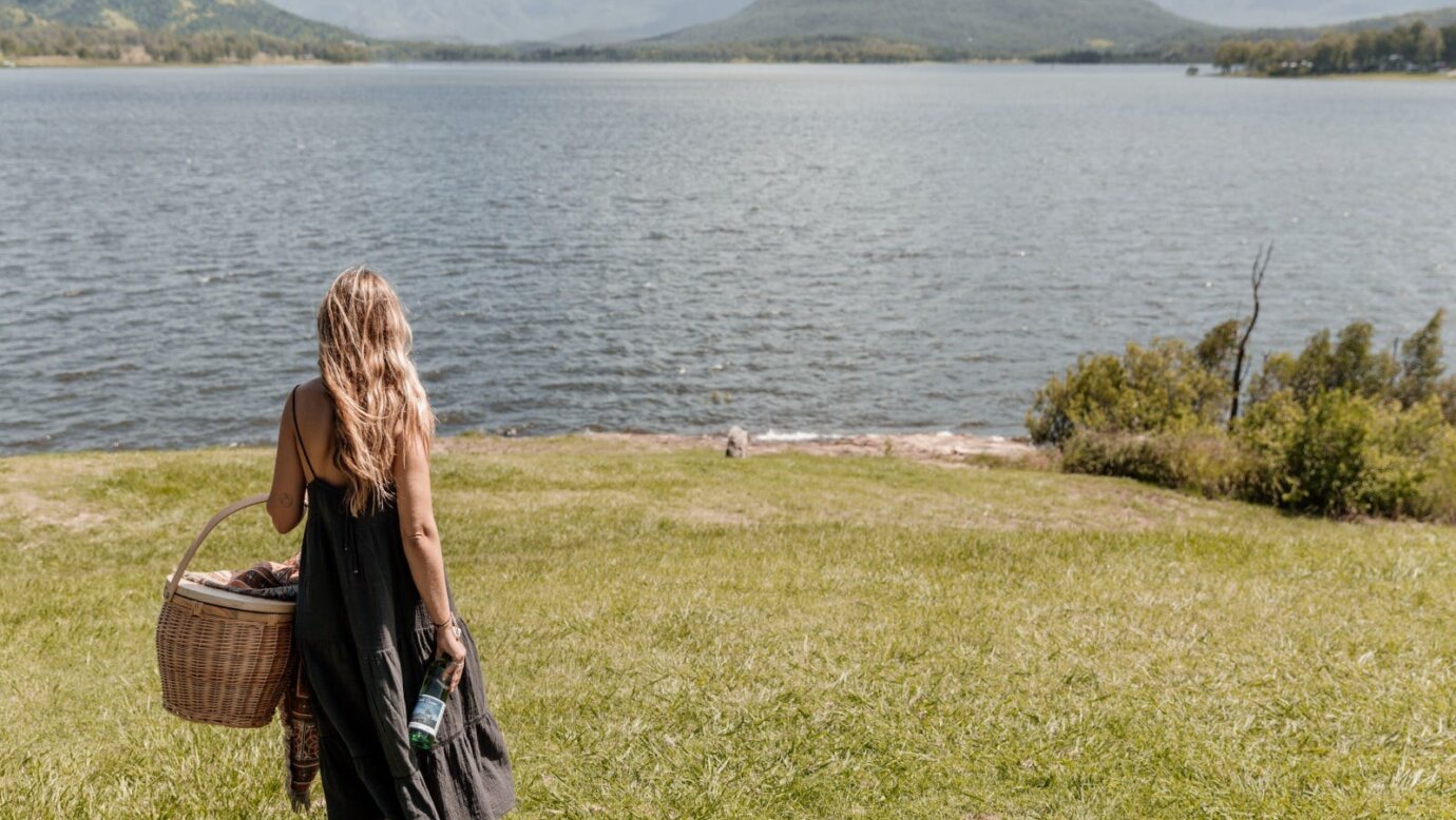 A woman walks towards the edge of a lake carrying a picnic basket