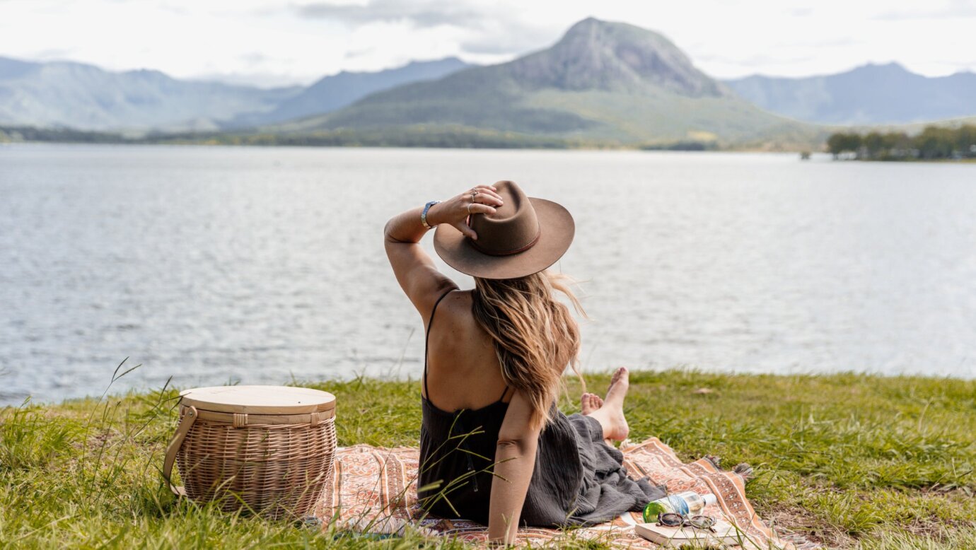 A woman sits on a picnic rug looking across a lake to the distant mountain