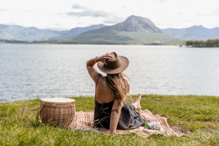 A woman sits on a picnic rug looking across a lake to the distant mountain