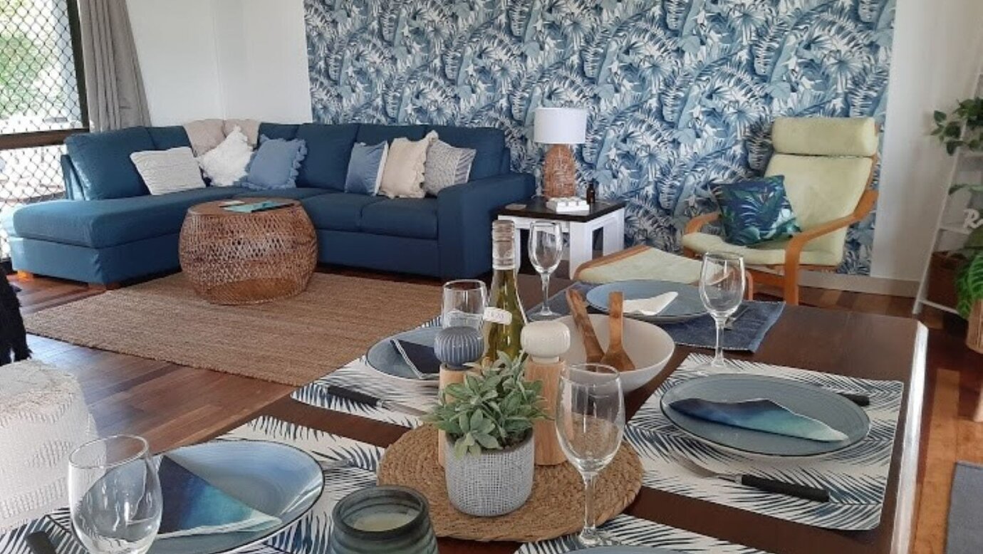 open plan living dining area with table set for 6. In the background is the comfortable lounge