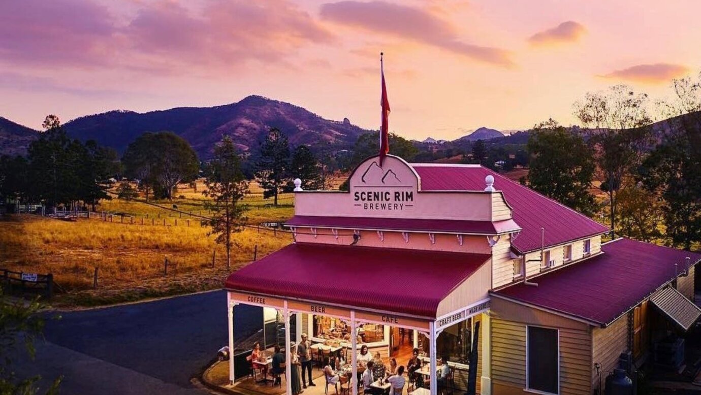 A small historic building set among fields with a mountain range behind