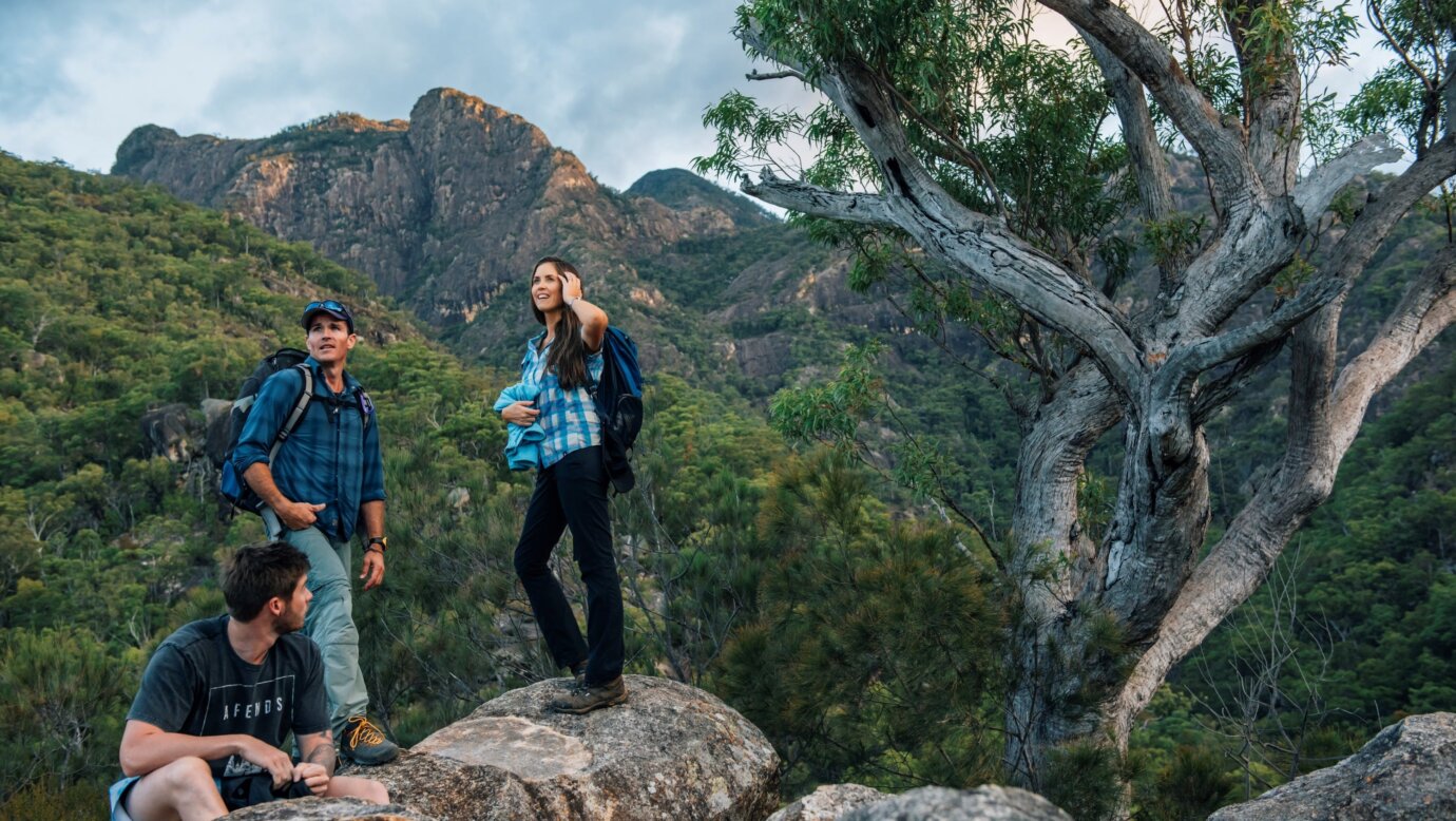 Three hikers stand on large boulders with a mountain range behind them
