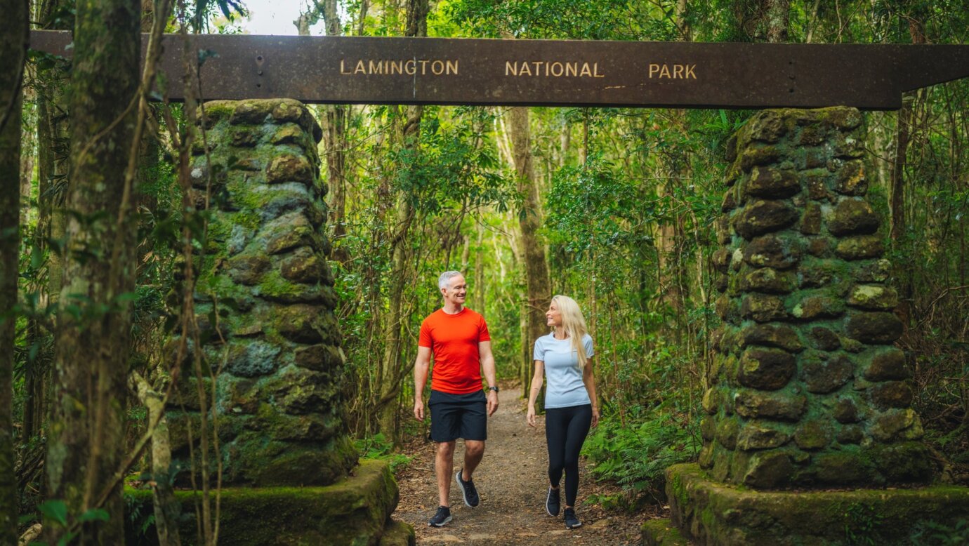 A man and woman walk through the arch at the start of a walk in a national park rainforest