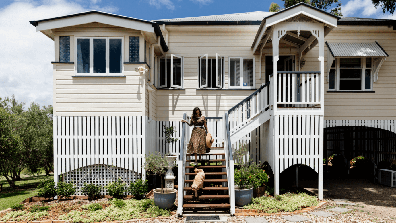 A woman and a dog walk up the front staircase of a historic Queenslander house stay