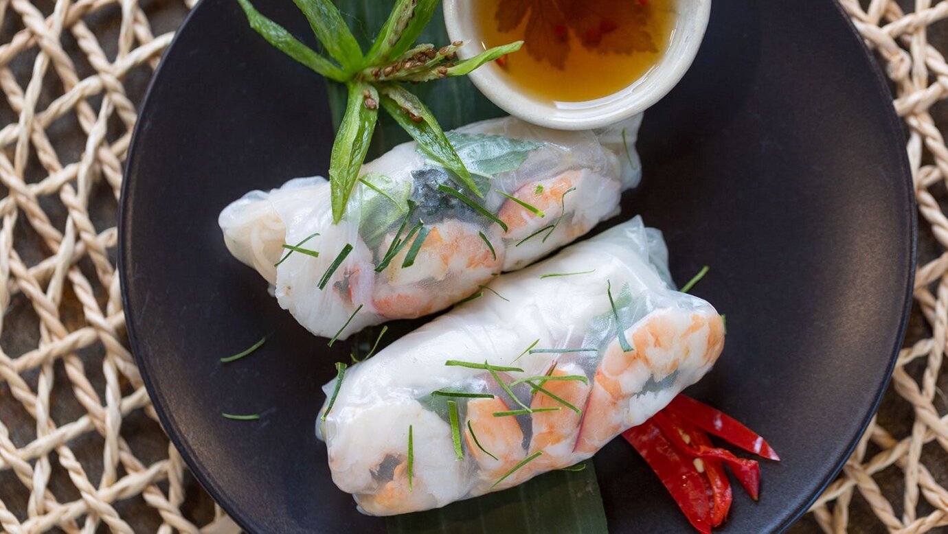 Rice paper rolls on a black plate with dipping sauce