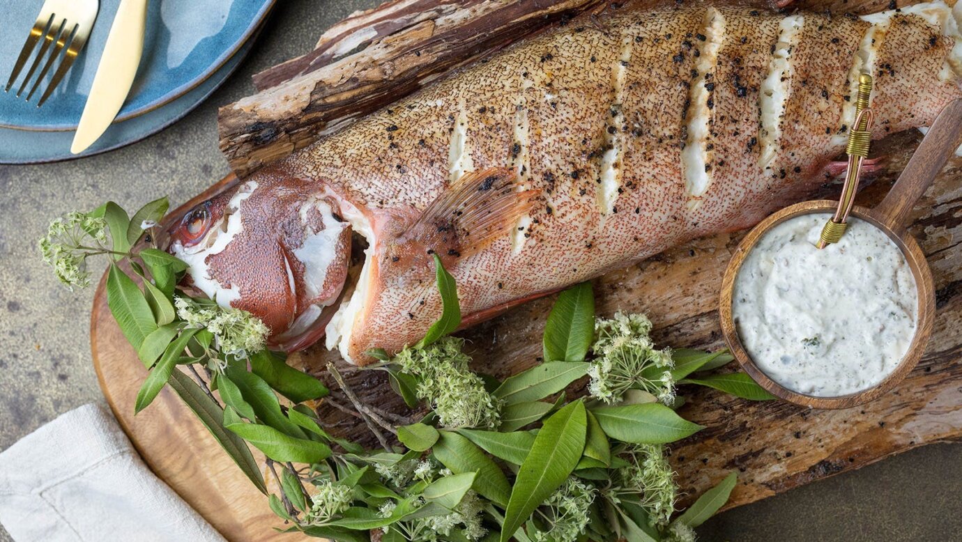 Cooked fish on a wooden chopping board with greens