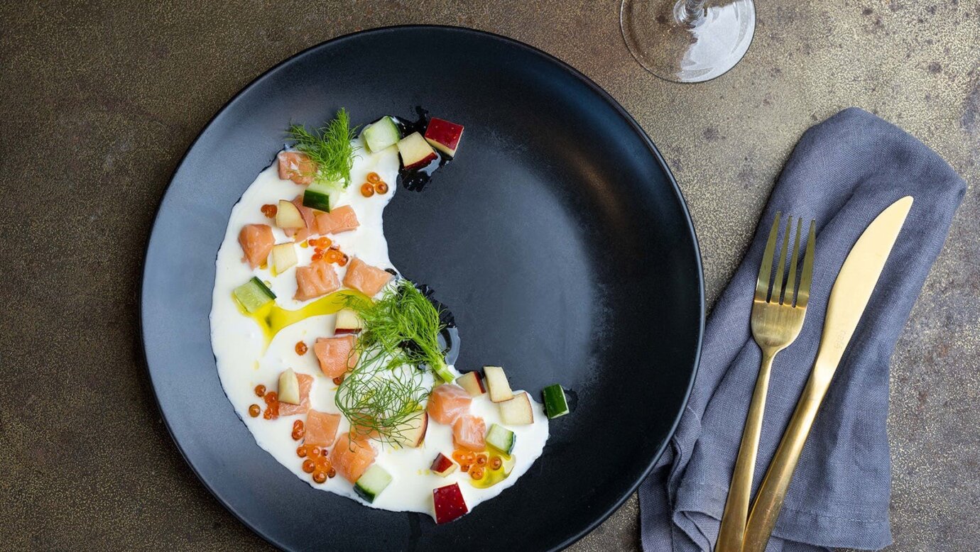 Cured trout on a black plate with wine and cutlery