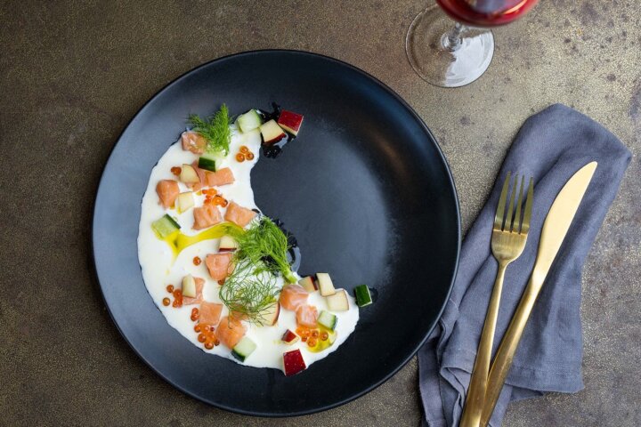 Cured trout on a black plate with wine and cutlery