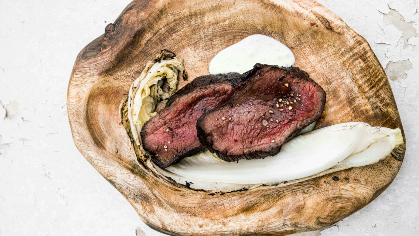 Dry-aged local Black Angus rib eye, wilted wombok and smoked macadamia served on a rustic wood plate