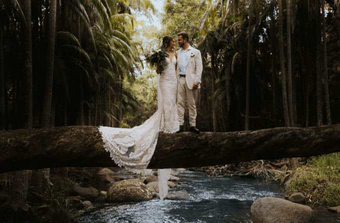 Married couple standing on a natural tree log bridge over a creek at Tamborine Mountain Glades.