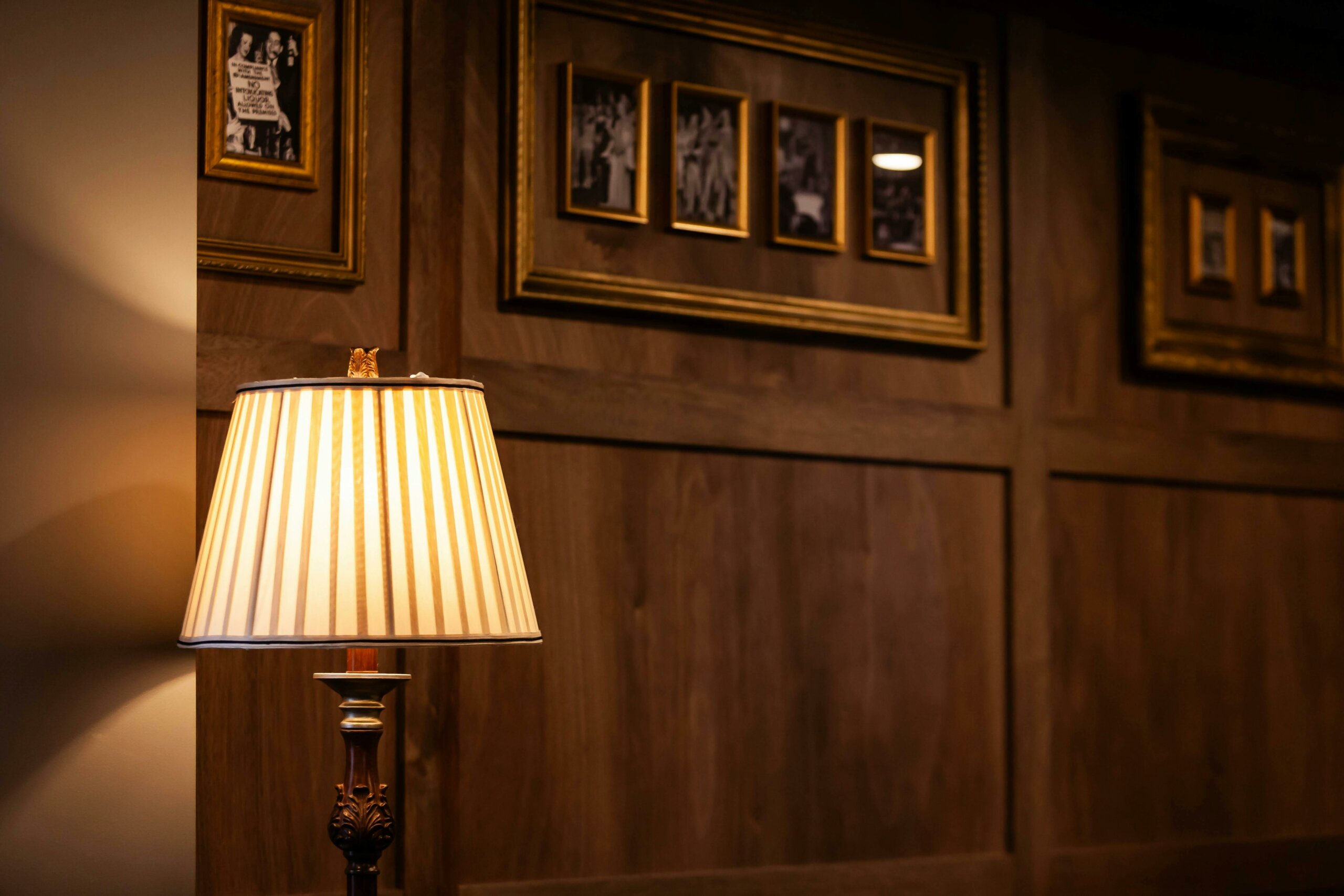 A lamp in front of a wooden panelled wall with historical photographs and art