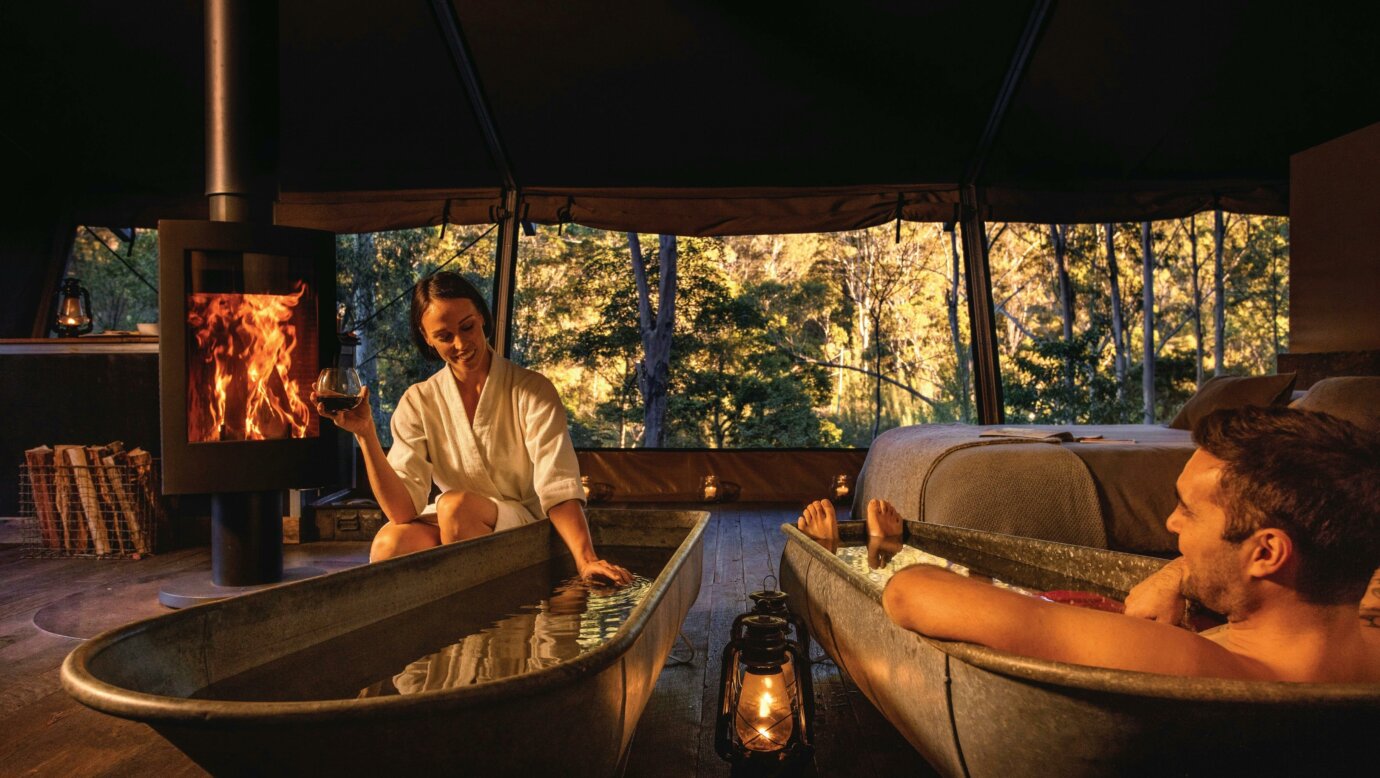 Couple enjoying bath by the fire inside safari tent with view to the natural environment.